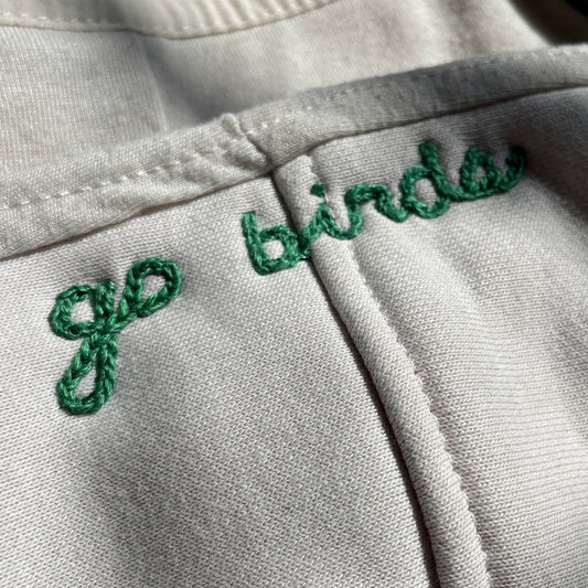 Embroidered text 'go birds' on a cream fabric background