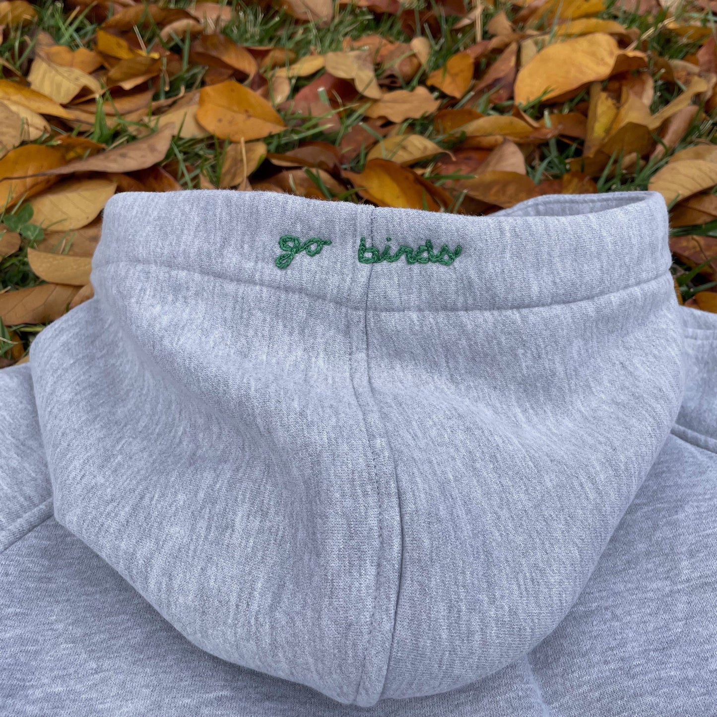 Gray sweatshirt with 'go birds' embroidery on a grassy background
