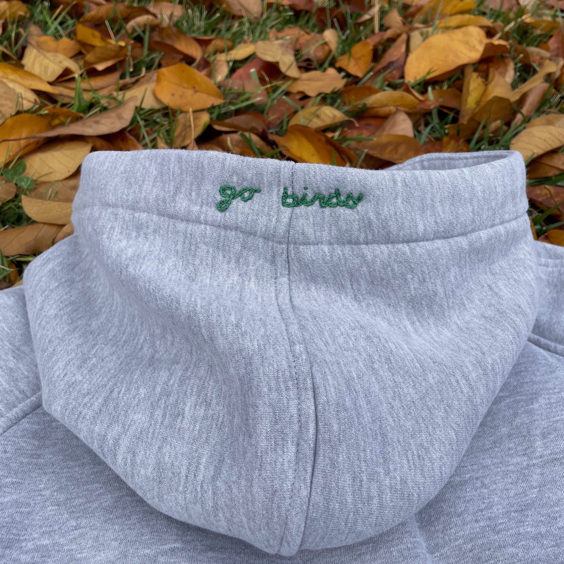 Gray sweatshirt with 'go birds' embroidery on a grassy background