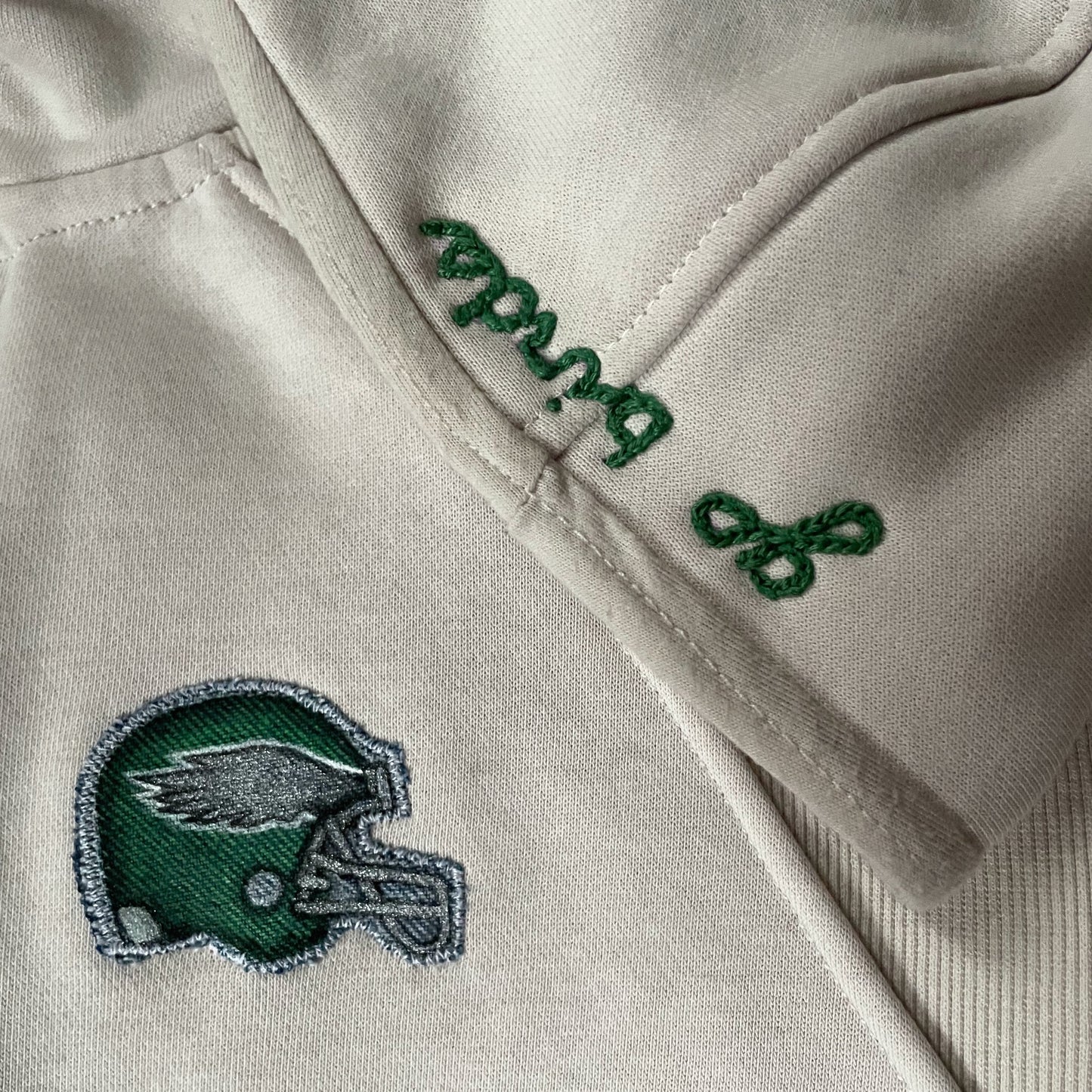 Close-up of a cream jacket with green embroidered text and logo.