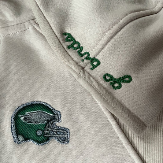 Close-up of a cream jacket with green embroidered text and logo.